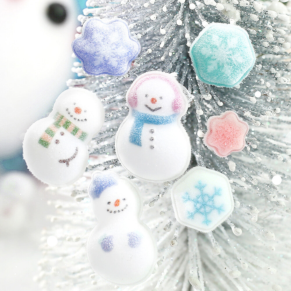 Three white snowman-shaped stickers with colorful scarves and faces, plus three snowflake-shaped stickers in pastel blue, pink, and mint, displayed on a white glittery Christmas tree.