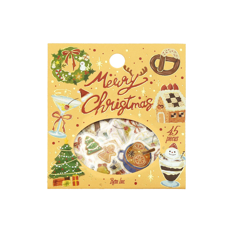 A Christmas-themed sticker pack in a decorative yellow sleeve with illustrations of ornaments, a gingerbread house, a martini glass, and the words 'Merry Christmas.' A circular window reveals assorted stickers inside.