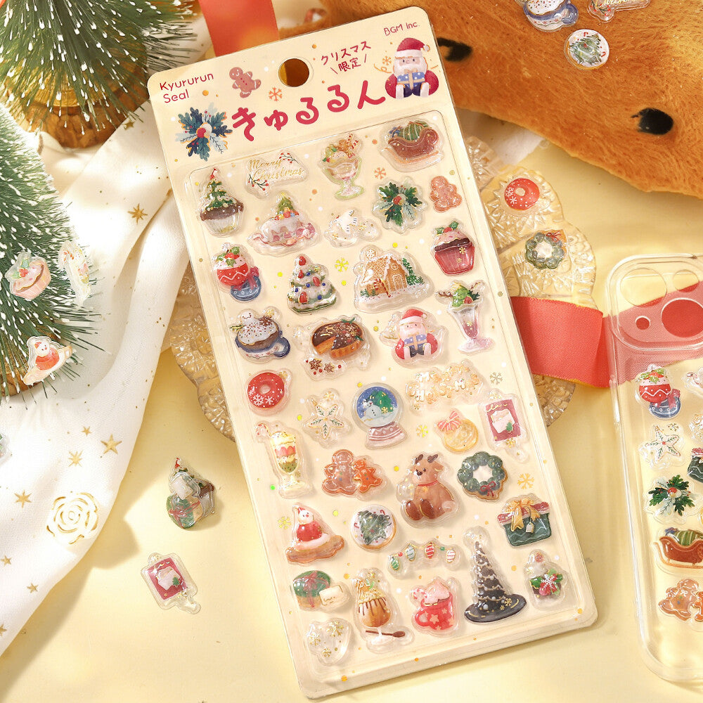 A sheet of small Christmas-themed stickers on a beige backing card, shown against a decorated winter theme background.