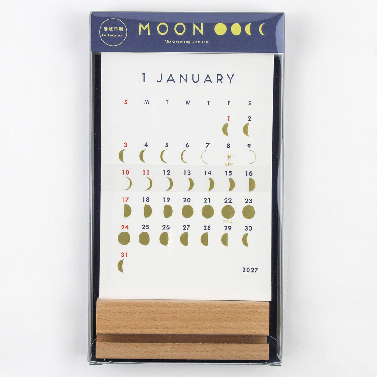 A boxed January 2027 calendar featuring a white page with a moon phase grid and dates, in a dark navy package with gold moon illustrations and a small wooden stand visible at the bottom.