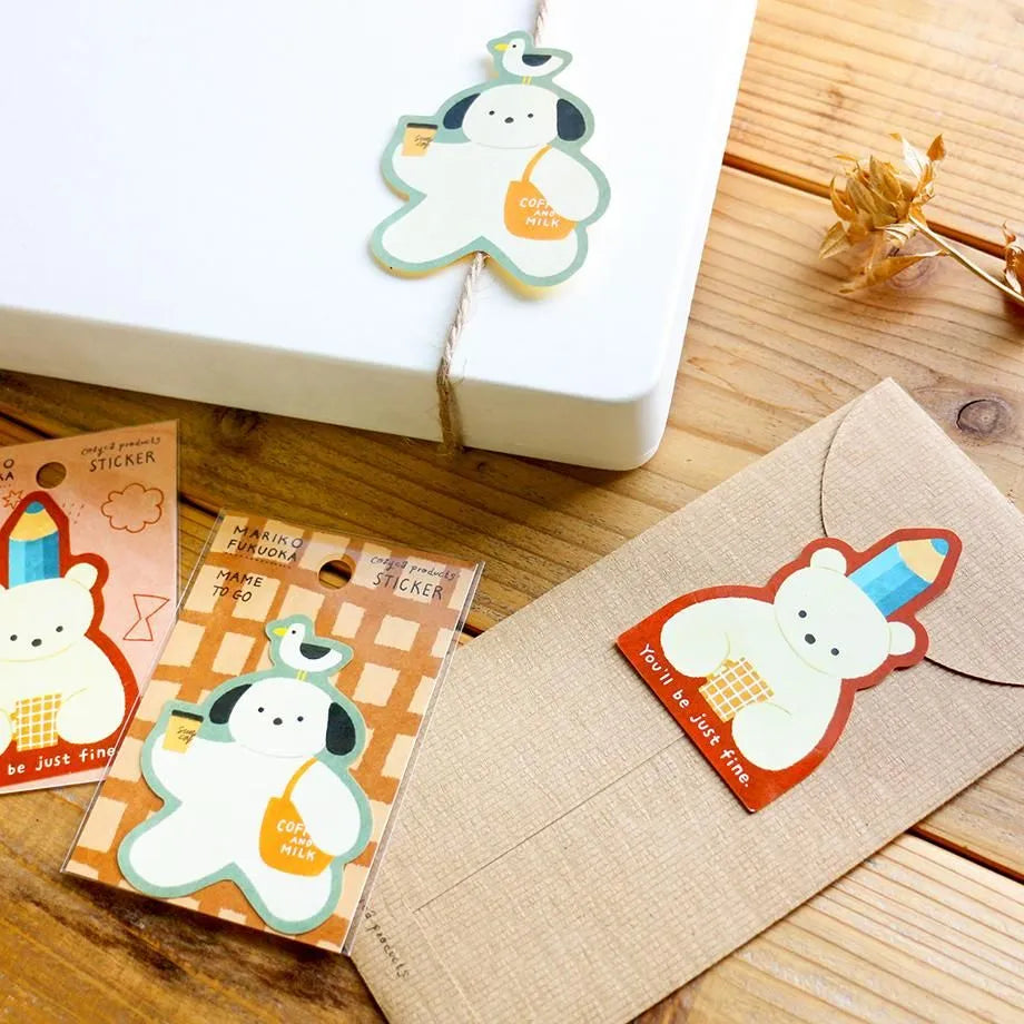 Kawaii-style sticker set featuring a cute cartoon bear character, shown with its packaging and applied to a kraft paper envelope on a wooden tabletop.