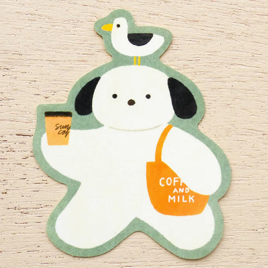 A die-cut sticker featuring a white cartoon dog with black ears, a green outline, a small bird on its head, and an orange bag reading 'COFFEE AND MILK,' while holding an orange coffee cup. The item is photographed on a light wood surface.