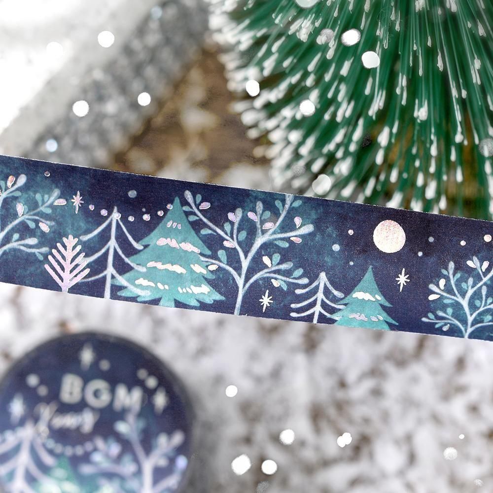 A navy decorative washi tape strip with a winter tree illustration shown next to a snowy pine tree