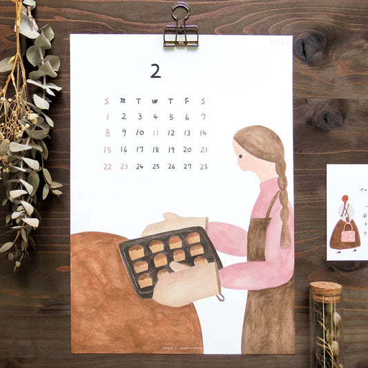 Calendar with illustration of a woman baking, pinned to a wooden board with decorative elements.