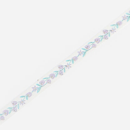 A close-up of slim masking tape featuring a delicate repeating pattern of small lavender flowers and light blue-green leaves, set against a plain light gray background.