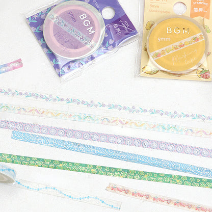 Several rolls of decorative washi tape are laid out on a white surface, showing pastel floral and geometric patterns in blue, green, pink, purple, and yellow. Two packaged rolls are visible at the top, labeled BGM 5mm.