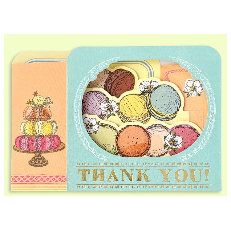 A pastel thank-you card featuring illustrated macarons in a circular window design and a stacked dessert illustration on the left, with the words “THANK YOU!” printed at the bottom.