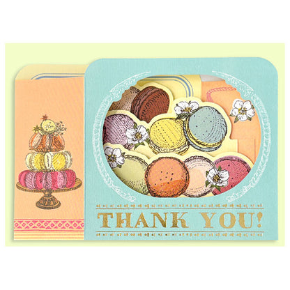 A pastel thank-you card featuring illustrated macarons in a circular window design and a stacked dessert illustration on the left, with the words “THANK YOU!” printed at the bottom.
