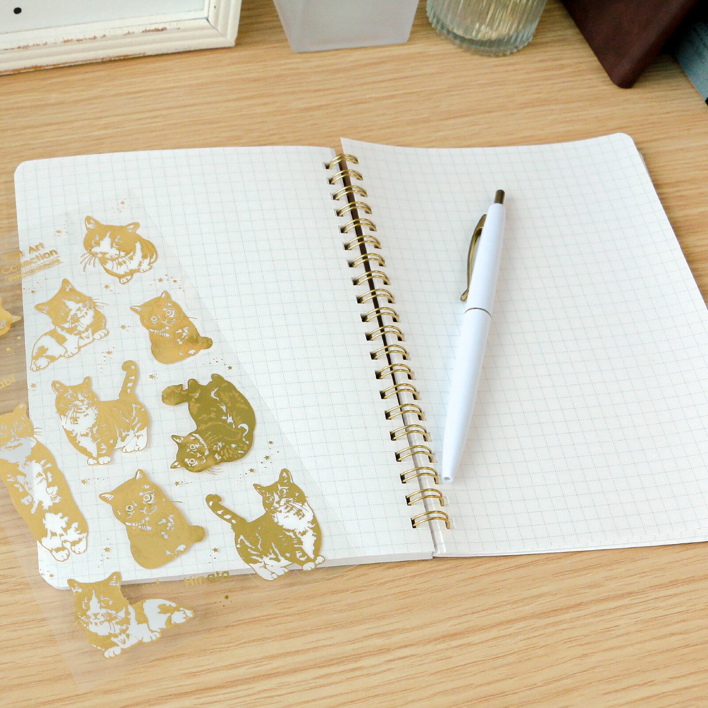 Open notebook with gold cat illustrations on one page and a pen on the other, on a wooden surface.