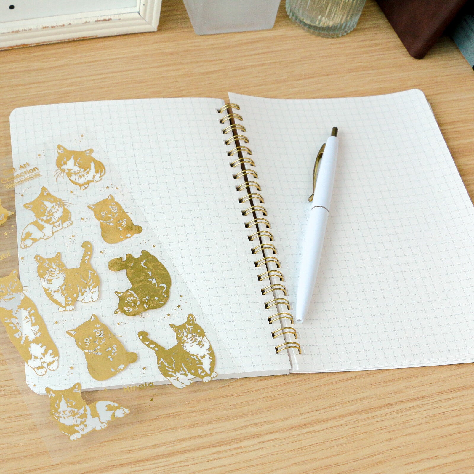 Open notebook with gold cat illustrations on one page and a pen on the other, on a wooden surface.