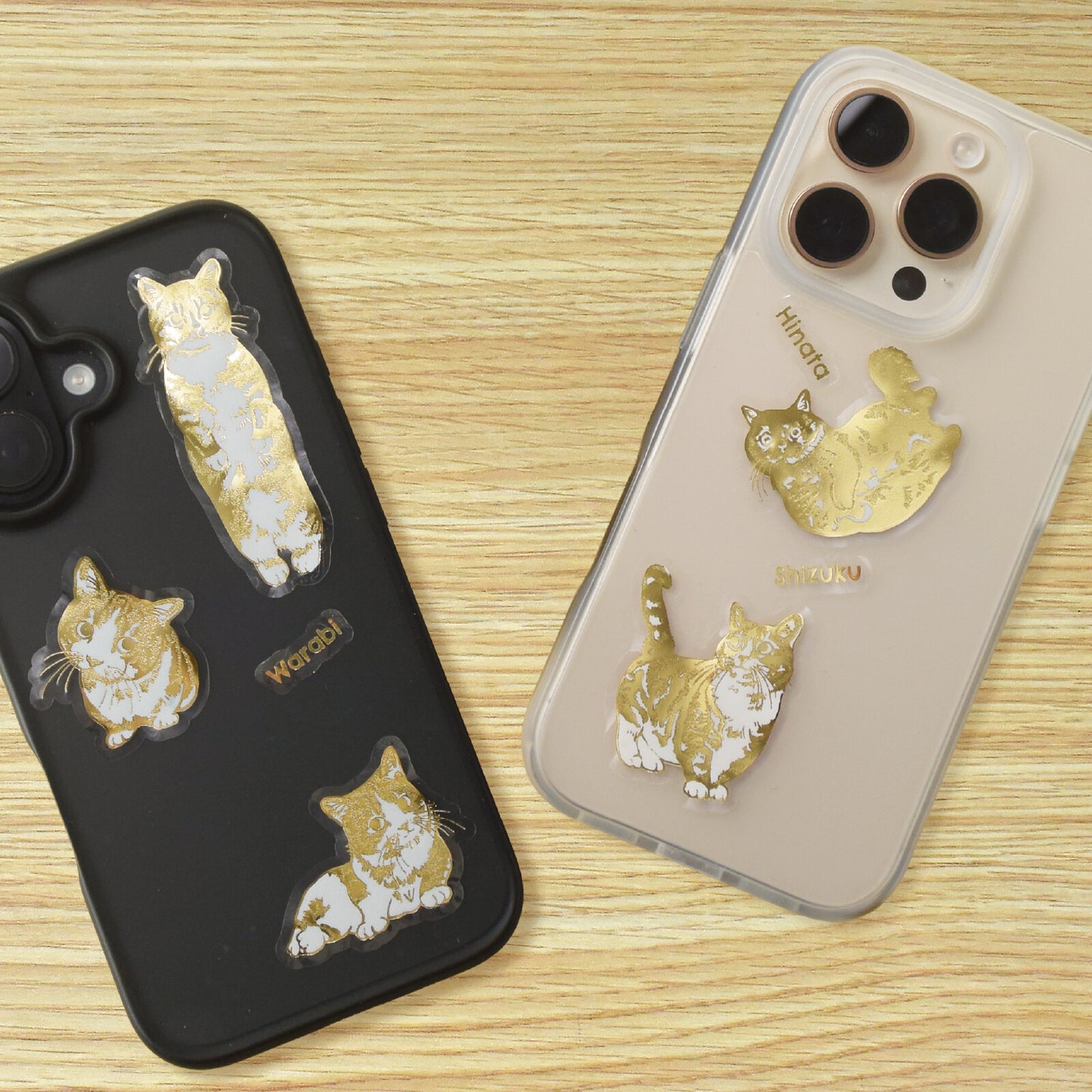 Two phone cases with gold cat sticker designs on a wooden surface
