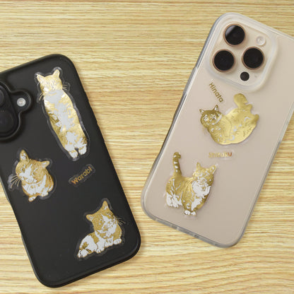 Two phone cases with gold cat sticker designs on a wooden surface