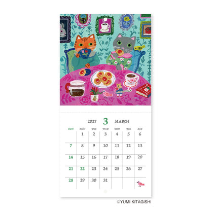 A vertical wall calendar page featuring a colorful illustration of two cats sitting at a table with tea and sweets, above a printed March 2027 calendar grid. The artist name YUMI KITAGISHI appears at the bottom.