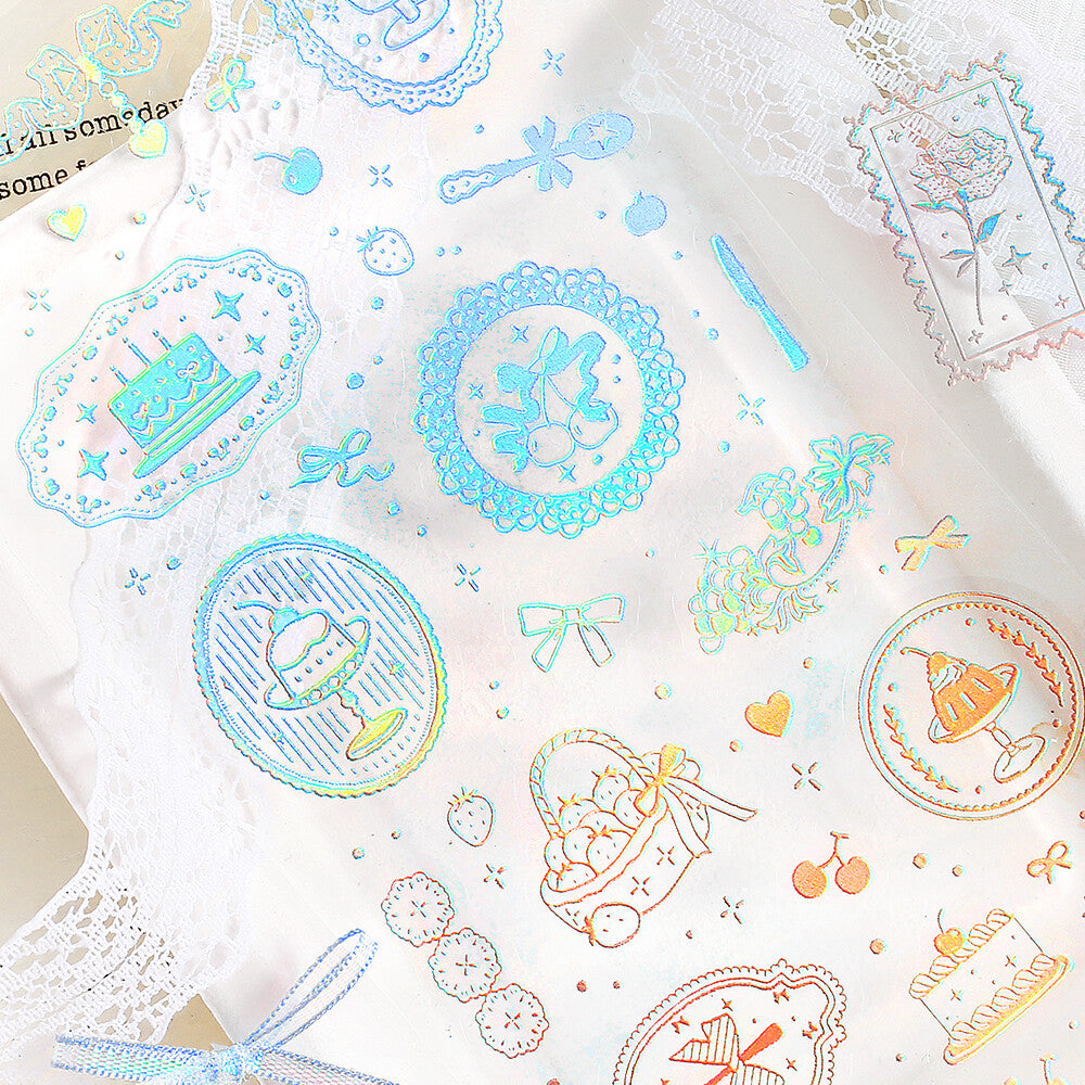Sticker sheet pastel iridescent printed motifs including cakes, bows, stars, strawberries, and decorative frames, photographed flat on a light surface.