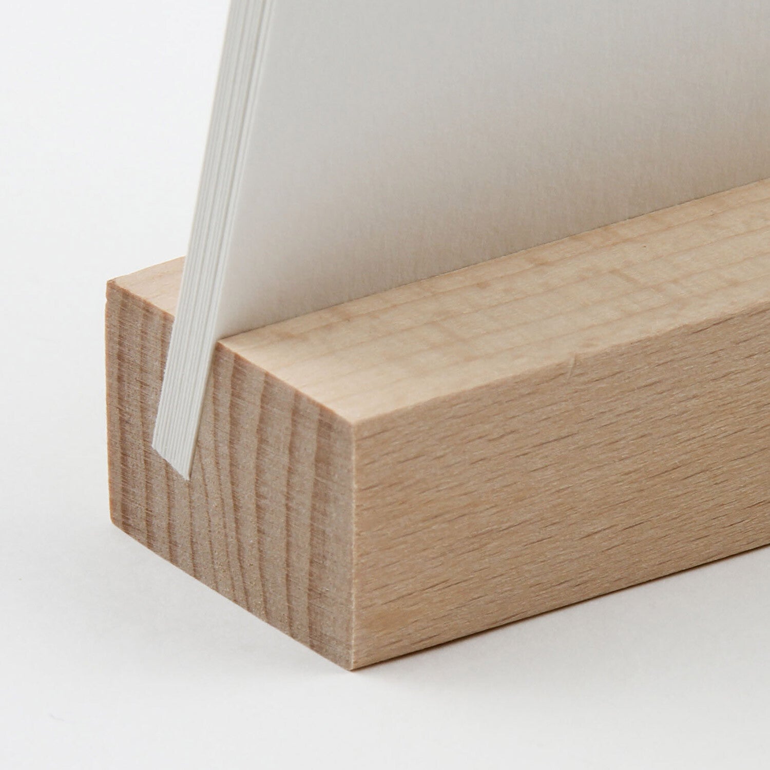 A close-up of a light natural wood rectangular block with the calendar pages partially inserted into its top slot, photographed on a clean white background.