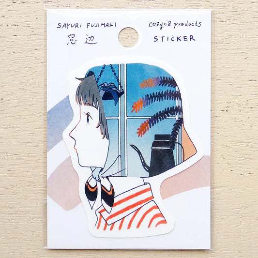 A die-cut sticker on a white backing card, featuring an illustrated side profile of a girl with dark hair and an orange-and-white striped shirt, with a blue window scene and plant inside her head. The card reads 'SAYURI FUJIMAKI Cozya products STICKER' and is photographed on a light wood surface.