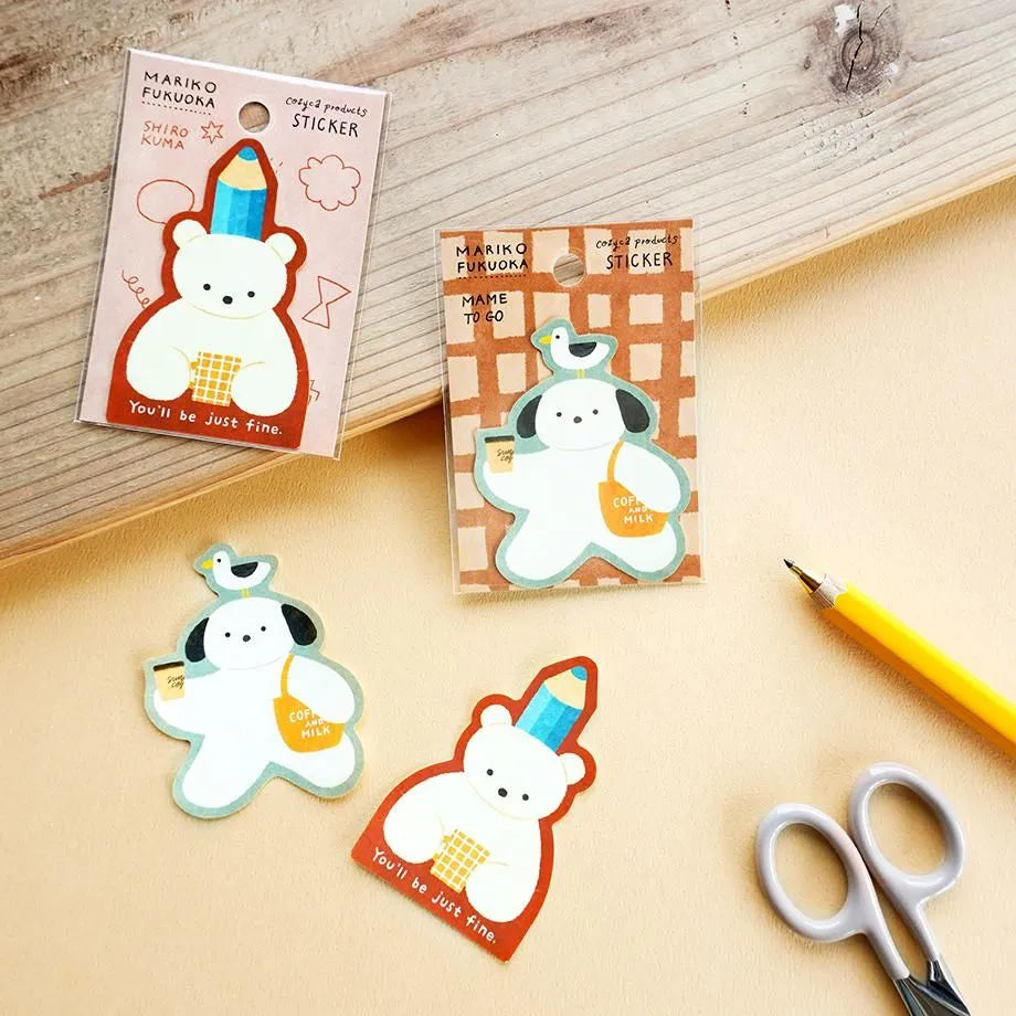 Three cute die-cut stickers featuring a white bear character with different colored outlines and accessories, displayed on a beige surface alongside a wooden board, scissors, and a yellow pencil.