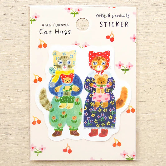 A die-cut sticker featuring two illustrated cats hugging, displayed on its original backing card. The backing card has a cream background decorated with cherry blossom motifs and reads 'AIKO FUKAWA Cat Hugs' and 'Cozyca products STICKER'.