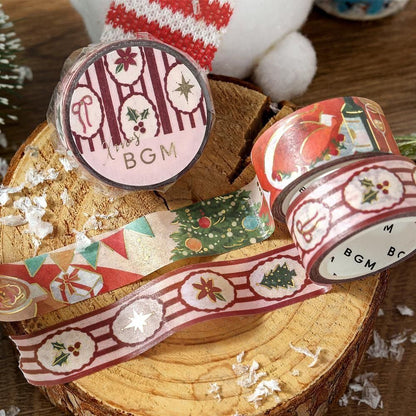 Christmas-themed decorative washi tape rolls displayed on a rustic wood slice, featuring holiday patterns like pine trees, ornaments, stars, and gift boxes in red, green, cream, and gold tones.