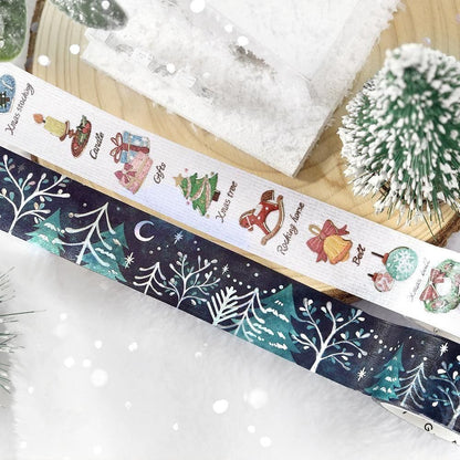 A navy decorative washi tape strip with a winter tree illustration next to another washi tape with various Christmas themed patterns.