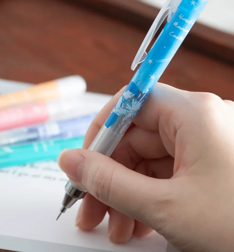 A hand holding a blue and silver mechanical pencil with a Howl's Moving Castle design, writing on a piece of paper.