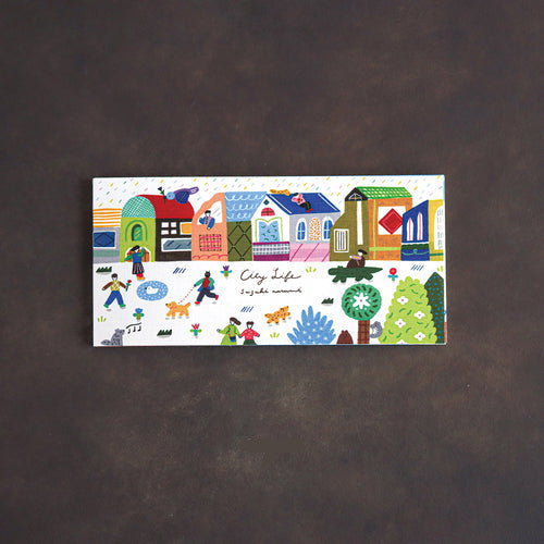 A rectangular notepad featuring a colorful hand-drawn illustration of houses, people, dogs, and trees, with the text 'City life'. Displayed on a dark brown textured background.