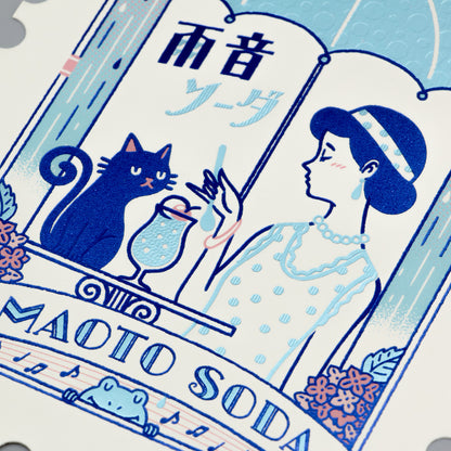 Stylized illustration of a woman, cat, and umbrella with 'AMADO SODA' text on a foil-stamped postcard.