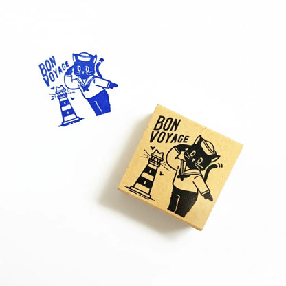 Wooden block with 'Bon Voyage' design featuring a cat and lighthouse, next to blue illustration of the same design.