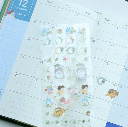 A sheet of cute planner stickers featuring Totoro and friends, displayed on an open monthly calendar.