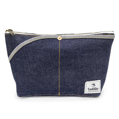 A dark blue denim zippered pouch with a silver zipper, a central gold-tone snap button, and a white 'Luddite' brand patch on the bottom right, shown against a plain white background.