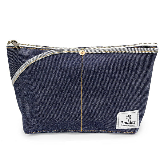 A dark blue denim zippered pouch with a silver zipper, a central gold-tone snap button, and a white 'Luddite' brand patch on the bottom right, shown against a plain white background.