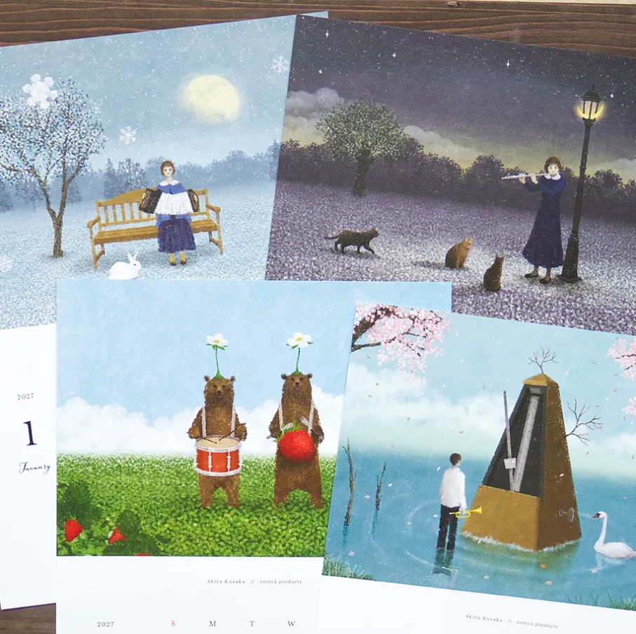 Four illustrated calendar pages arranged on a dark wooden surface. The prints feature whimsical scenes: a woman reading in a snowy landscape, a woman with a flute in a starry field at night, two bears playing drums in a grassy field, and a man standing near a large clock in a lake with a swan.