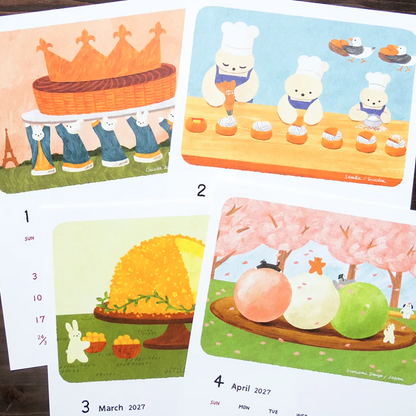 Four illustrated calendar pages laid out on a wooden surface, showing whimsical drawings of a basket and hat, small characters making pastries, a honeycomb, and fruit under pink cherry blossoms. Dates and days of the week are visible on the cards.