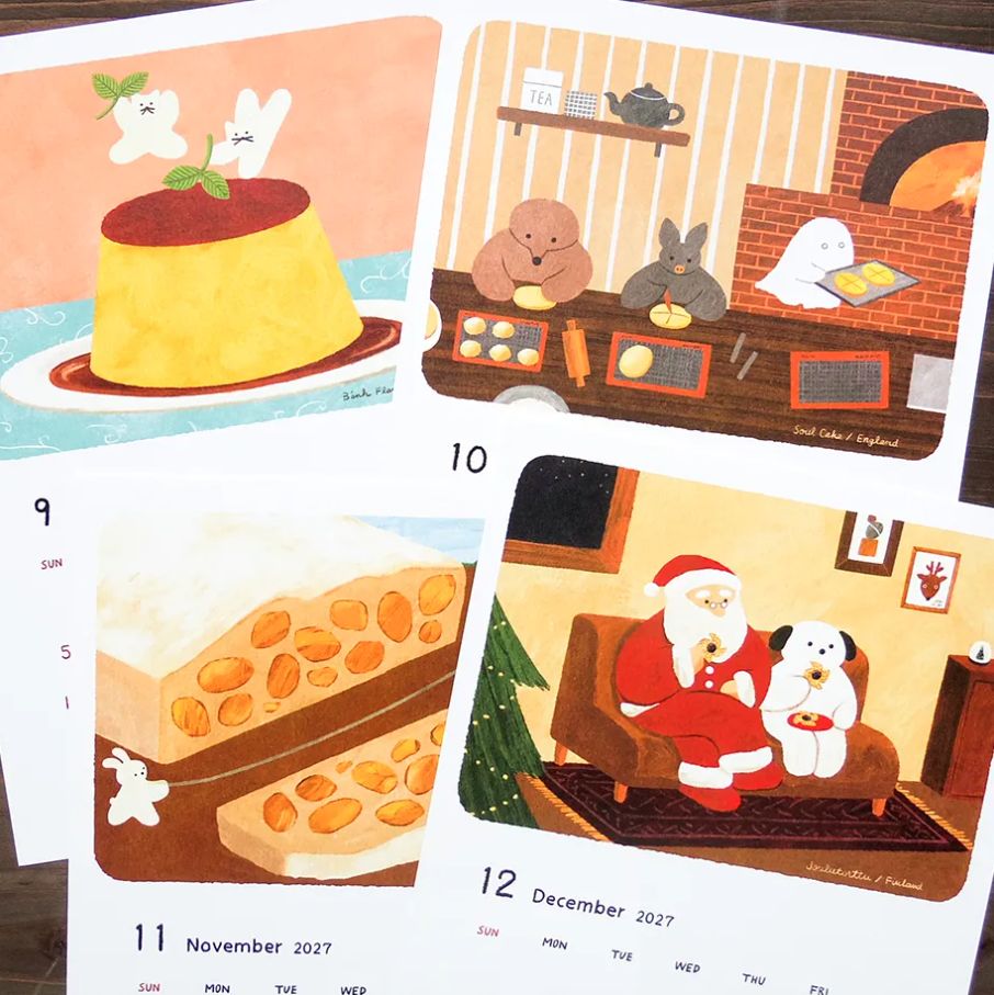 Four illustrated calendar pages laid on a dark wooden surface, showing whimsical holiday drawings including a yellow flan, rabbits at a fireplace, sliced cheese, and Santa Claus sitting with a white dog. Dates and days of the week are visible on the pages.