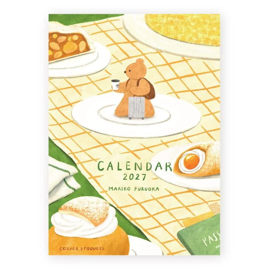 A 2027 calendar cover by Mariko Fukudaka, illustrated with a teddy bear on a table setting surrounded by pastries and a passport. The design features a warm yellow grid tablecloth, white plates, and various colorful food illustrations.