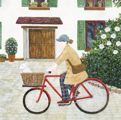 A watercolor-style illustration of a person riding a red bicycle with a wicker basket containing a white rabbit, set in front of a white house with green shutters and a large flowering bush.