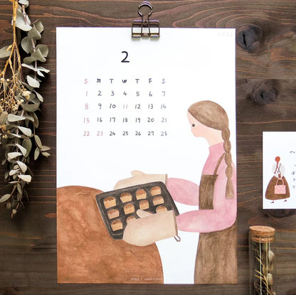 Calendar with illustration of a woman baking, pinned to a wooden board with decorative elements.